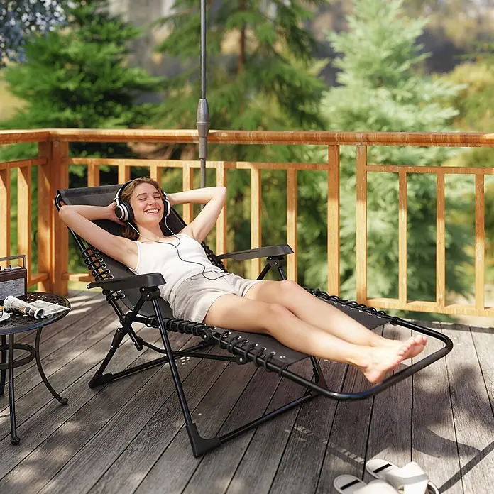 Outsunny Garten-Liegestuhl - Metall, Textelin, Klappbar, Schwarz, B x T x H: 65 x 160 x 112 cm - Eine Frau entspannt sich in einem dunkelgrauen Schwerelosigkeits-Liegestuhl auf einer Holzterrasse.
