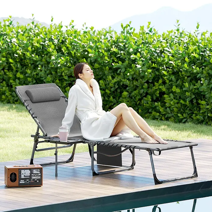 Furnicato Gartenliege - B x T: 60 x 190 cm, Grau, Kunststoff - Eine Frau entspannt auf einem grauen tragbaren Liegestuhl mit Beistelltisch auf einer Holzterrasse am Pool.