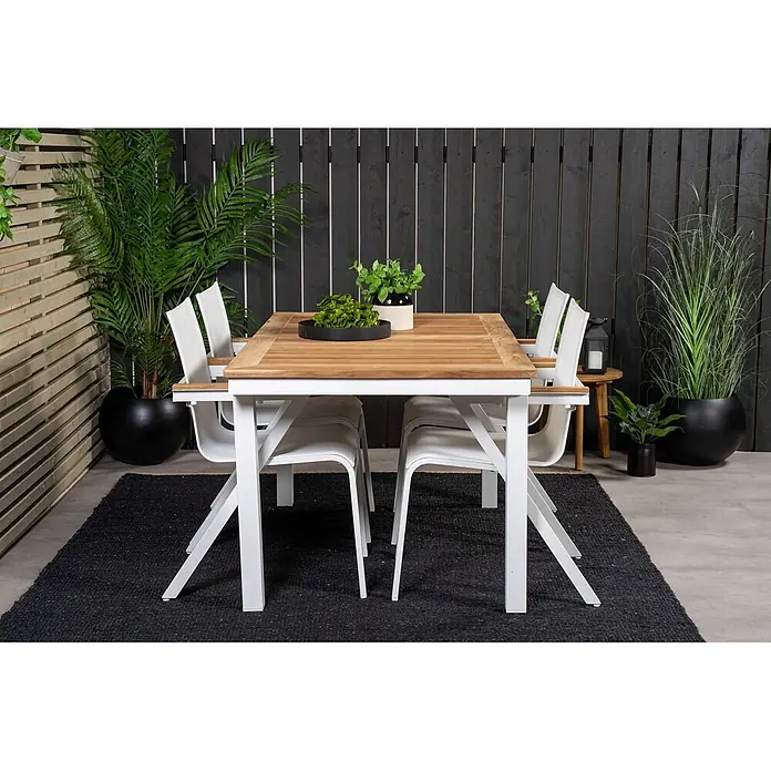 Ebuy24 Gartentisch Panama - L x B x H: 240 x 90 x 76 cm, Ø x H: 90 x 76 cm, Aluminium, Teak, Sonstige, Weiß - Outdoor-Essgruppe: ein Holztisch mit weißen Metallbeinen und passenden weißen Stühlen auf einem dunklen Teppich im Terrassenbereich.