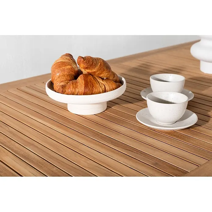 Ebuy24 Gartentisch Panama - L x B x H: 240 x 90 x 76 cm, Ø x H: 90 x 76 cm, Aluminium, Teak, Sonstige, Weiß - Goldene Croissants auf weißem Keramikständer und zwei weiße Keramiktassen mit Untertassen auf Holztisch.