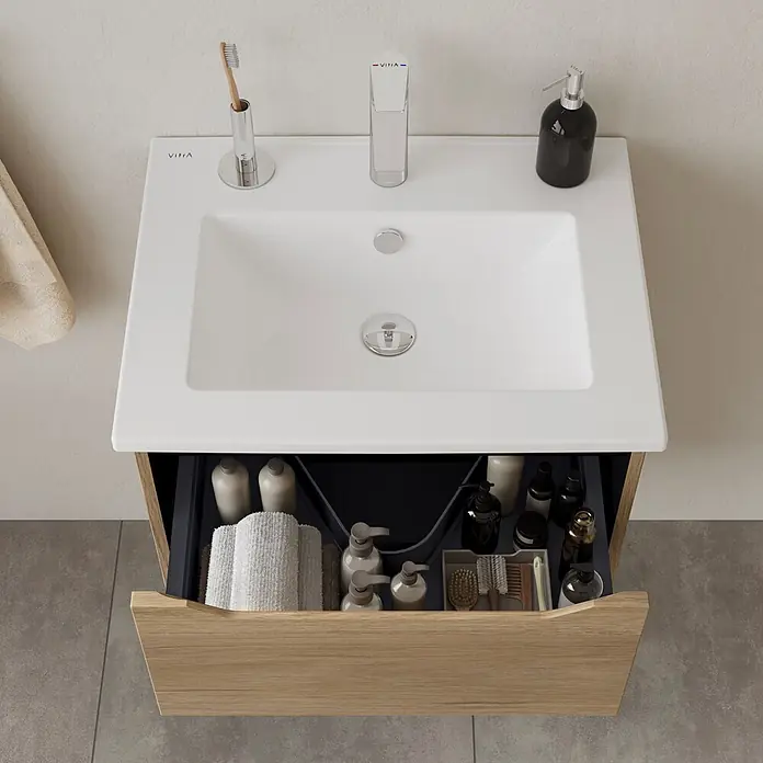VitrA Integra Square Badmöbel-Set - Gesamtbreite Badmöbel: 60 cm, Eiche Gold - Weiße Keramikspüle auf hellem Holzwaschtisch mit geöffneter Schublade, die organisierte Toilettenartikel zeigt.