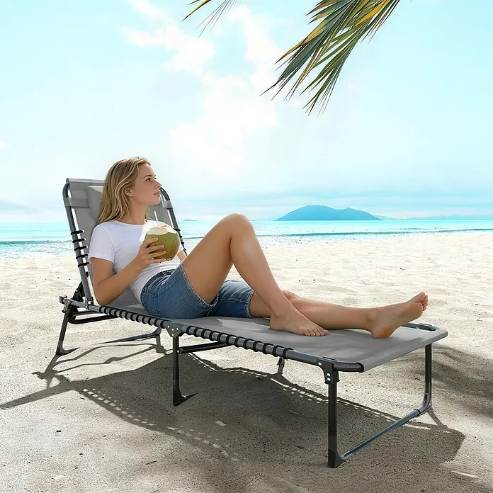 Outsunny Gartenliege - B x T: 58 x 189 cm, Grau, Stahl, Klappbar - Graues Stoff-Strandbett mit dunklem Rahmen, von einer Frau zum Entspannen am Sandstrand genutzt.
