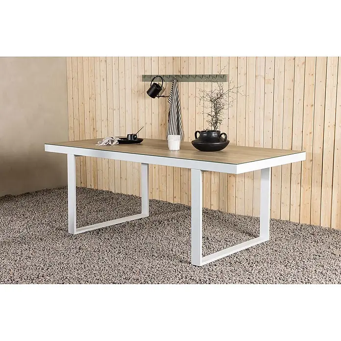 Ebuy24 Gartentisch Merlo - L x B x H: 200 x 90 x 75 cm, Ø x H: 90 x 75 cm, Aluminium, Weiß - Gartentisch mit weißem Gestell und Holzoptikplatte mit Glasauflage auf Kies vor Holzwand.