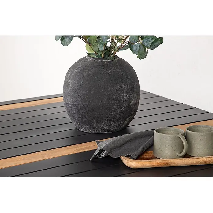 Ebuy24 Gartentisch Togo - L x B x H: 150 x 90 x 75 cm, Ø x H: 90 x 75 cm, Aluminium, Sonstige, Schwarz - Schwarzer Lamellentisch mit Holzstreifen, dekoriert mit einer dunklen Vase mit Grünzeug, zwei Tassen und einer Serviette auf einem Holztablett.