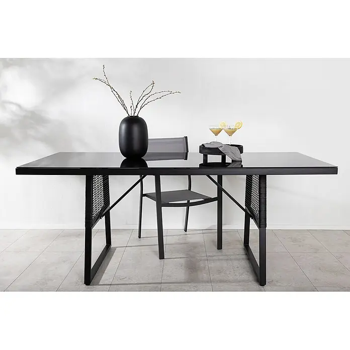Ebuy24 Gartentisch Dallas - L x B x H: 193 x 90 x 77 cm, Ø x H: 90 x 77 cm, Aluminium, Glas, Sonstige, Schwarz - Schwarzer Outdoor-Esstisch mit Glasplatte und Metallgestell, mit geflochtenen Details, daneben ein passender Stuhl.