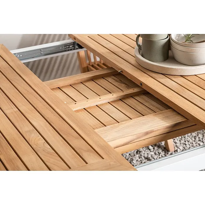 Ebuy24 Gartentisch Panama - L x B x H: 324 x 100 x 75 cm, Ø x H: 100 x 75 cm, Aluminium, Teak, Sonstige, Weiß - Ausziehbarer Teakholz-Tisch, teilweise geöffnet, zeigt den Ausziehmechanismus und die Lattenoberfläche. Geschirr steht auf einem Ende.