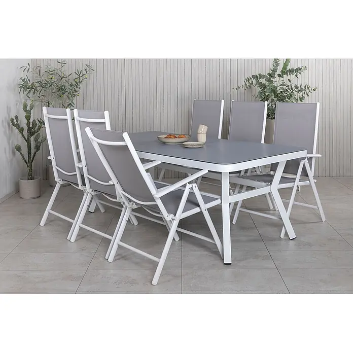 Ebuy24 Gartentisch Massa - L x B x H: 200 x 100 x 74 cm, Ø x H: 100 x 74 cm, Aluminium, Glas, Schnur, Sonstige, Weiß - Outdoor-Esstischgarnitur mit weißem Metalltisch und sechs grauen Klappstühlen auf einer Terrasse.