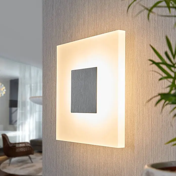 Lucande Wandleuchte Berlind - L x B x H: 6 x 26 x 26 cm, weiß / opal - Moderne quadratische Wandleuchte mit gebürstetem Silberakzent, die ein warmes Licht auf eine strukturierte Wand in einem Wohnraum wirft.