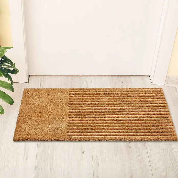 Fußmatte Coco Shape - 75 x 45 cm, Natur, Material Nutzschicht: 100 % Kokos, Streifen - Braune Kokosfasermatte mit glattem und gerilltem Bereich vor einer weißen Tür auf hellem Holzboden.