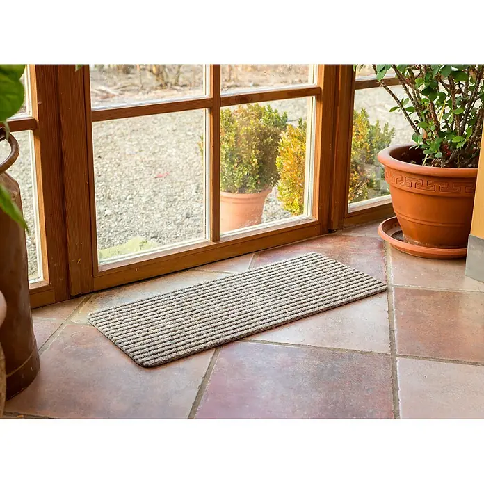 Fußmatte Rib Line Mini Sprint - 60 x 25 cm, Beige, Material Nutzschicht: 75 % Polypropylen, 25 % Polyester - Rechteckige, gestreifte hellgraue Fußmatte auf Terracottafliesen vor einer Glastür mit Holzrahmen, neben Topfpflanzen.