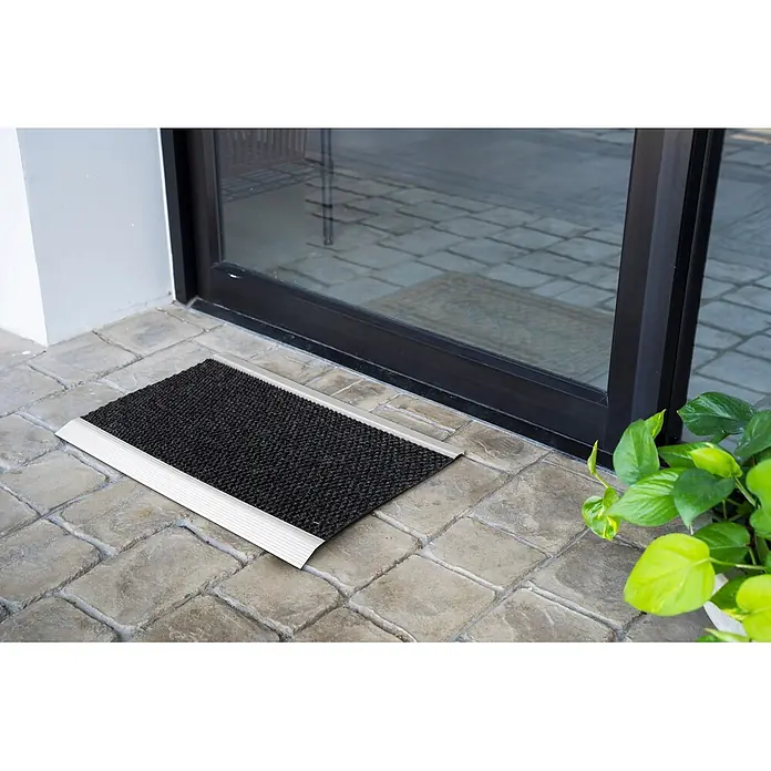 Fußmatte Aluminium - 80 x 60 cm, Anthrazit, Material Nutzschicht: 100 % Polypropylen - Schwarze Fußmatte mit silbernen Aluminiumkanten vor einer Glastür auf gepflastertem Untergrund.