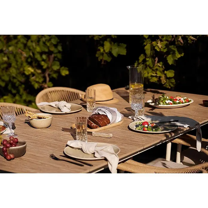 Ebuy24 Gartentisch Bella - L x B x H: 200 x 100 x 74 cm, Ø x H: 200 x 74 cm, Nonwood (PE), Aluminium, Sandfarben - Ein gedeckter Esstisch im Freien mit Tellern, Gläsern und Speisen für eine Mahlzeit im Garten.