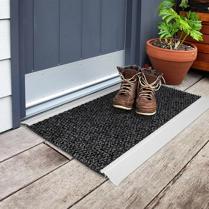 Fußmatte Aluminium - 80 x 60 cm, Anthrazit, Material Nutzschicht: 100 % Polypropylen - Schwarze Fußmatte mit silberner Übergangsschiene auf Holzterrasse vor einer Tür, dazu braune Stiefel.