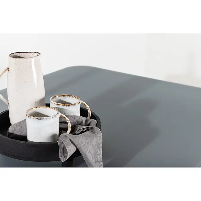 Ebuy24 Gartentisch Virya - L x B x H: 160 x 90 x 74 cm, Ø x H: 90 x 74 cm, Aluminium, Glas, Sonstige, Schwarz - Zwei Keramiktassen mit Bronzerändern und ein cremefarbener Keramikkrug auf einem dunklen Holztablett mit grauem Leinentuch.