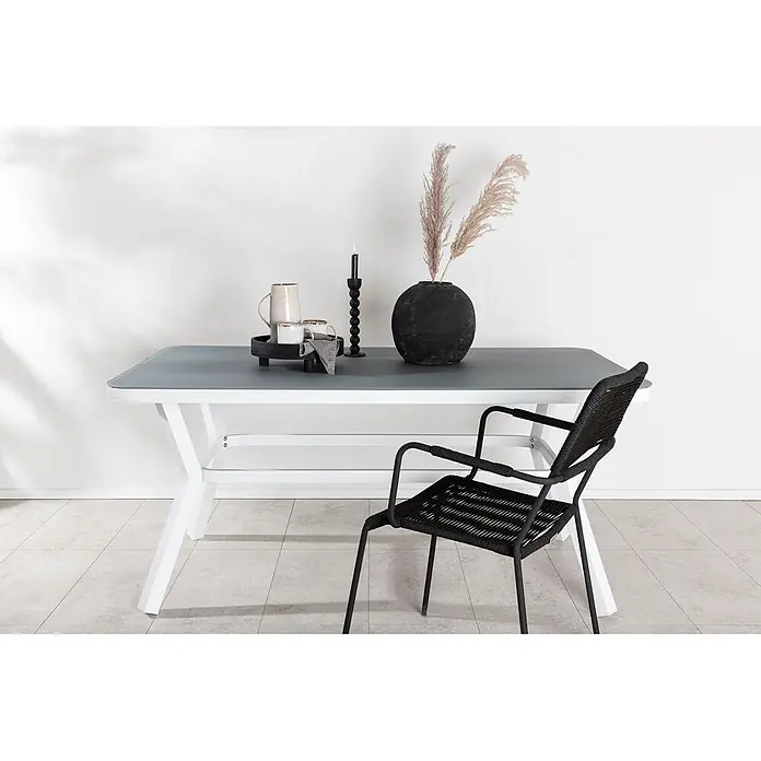 Ebuy24 Gartentisch Virya - L x B x H: 160 x 90 x 74 cm, Ø x H: 90 x 74 cm, Aluminium, Glas, Sonstige, Schwarz - Weißer Esstisch mit grauer Platte und schwarzem geflochtenem Sessel, arrangiert mit Dekoartikeln.