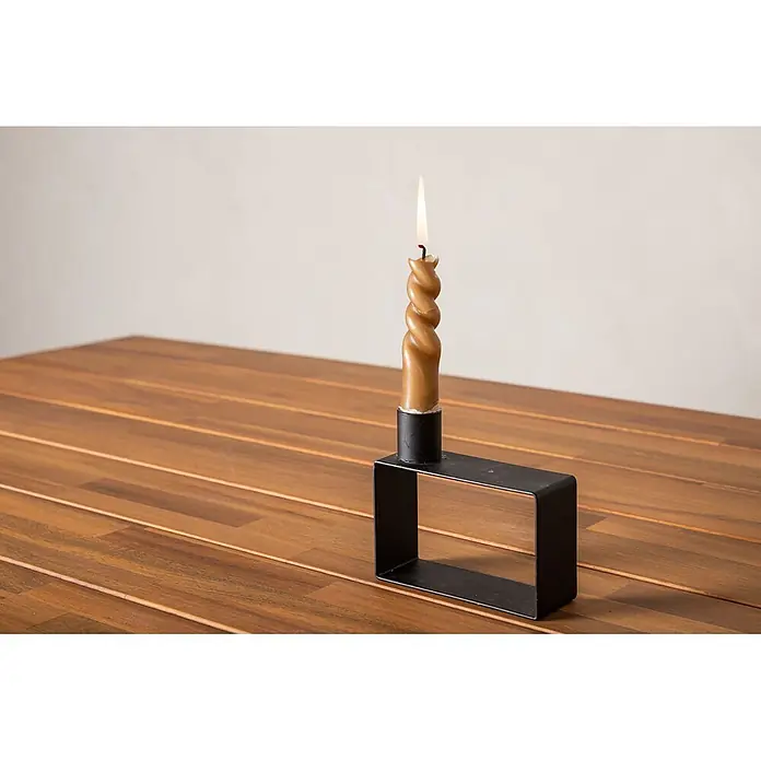 Ebuy24 Gartentisch Chan - L x B x H: 200 x 100 x 74 cm, Ø x H: 100 x 74 cm, Akazie, Stahl, Sonstige, Teak Dekor - Eine brennende gedrehte braune Kerze in einem schwarzen rechteckigen Metallkerzenhalter steht auf einem Holztisch.