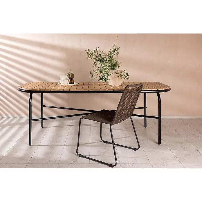 Ebuy24 Gartentisch Holmbeck - L x B x H: 200 x 90 x 75 cm, Ø x H: 90 x 75 cm, Akazie, Natur - Holztisch mit Lamellenplatte und schwarzem Metallrahmen, dazu ein brauner Flechtstuhl in einem Innenraum.