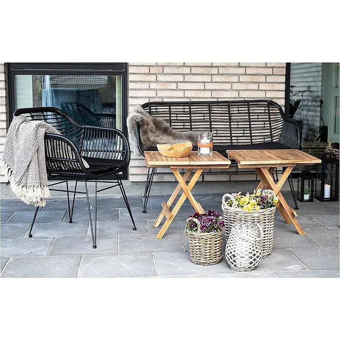 Ebuy24 Gartentisch Bine - L x B x H: 50 x 50 x 50 cm, Ø x H: 50 x 50 cm, Teakholz massiv, Sonstige, Braun - Schwarzer Outdoor-Sessel und Bank aus Korbgeflecht mit Holztischen auf einer Terrasse.