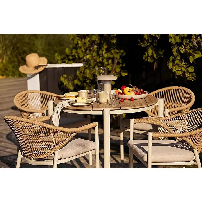 Ebuy24 Gartentisch Bella - L x B x H: 90 x 90 x 74 cm, Ø x H: 90 x 74 cm, Nonwood (PE), Aluminium, Sandfarben - Outdoor-Esstischgruppe: runder Holztisch und vier Stühle mit geflochtenen Rückenlehnen und beigefarbenen Polstern auf einer Terrasse.