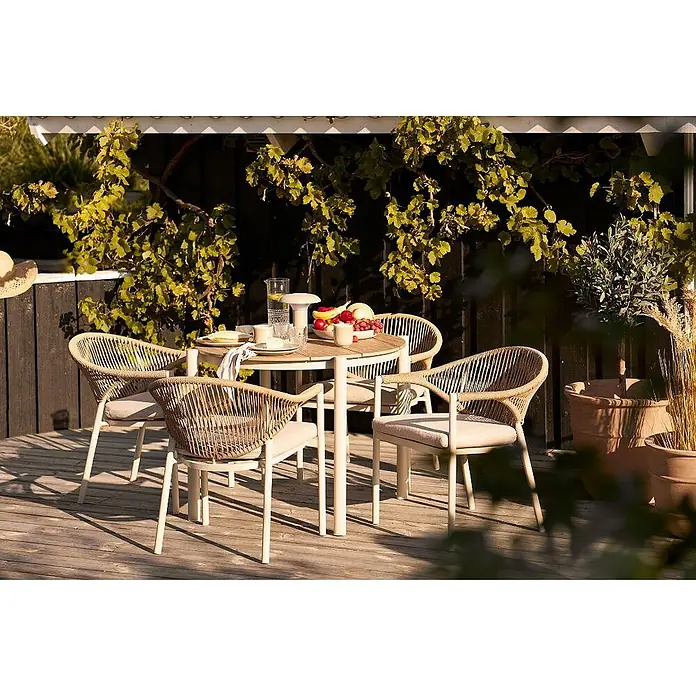 Ebuy24 Gartentisch Bella - L x B x H: 90 x 90 x 74 cm, Ø x H: 90 x 74 cm, Nonwood (PE), Aluminium, Sandfarben - Runder Gartentisch mit heller Holzplatte und cremefarbenen Beinen, dazu vier geflochtene beigefarbene Stühle mit Kissen, auf einer Holzterrasse.