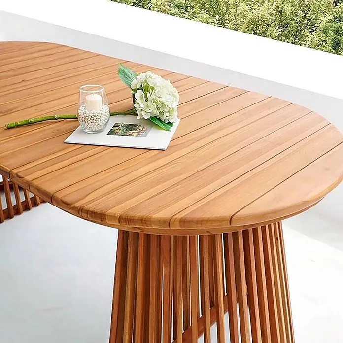 Ebuy24 Gartentisch Björk - L x B x H: 200 x 90 x 75 cm, Ø x H: 200 x 75 cm, Teak, Sonstige, Natur - Ovaler Holztisch mit Lattenfuß, im Außenbereich, dekoriert mit Blumen und einer Kerze.