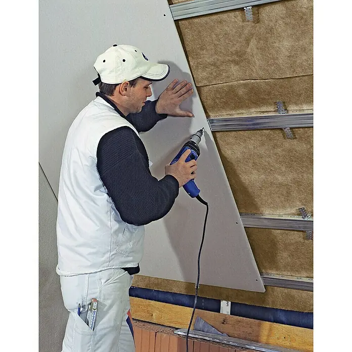 Knauf Gipskartonplatte Massiv GKF2.600 x 625 x 20 mm - Ein Handwerker befestigt eine Gipskartonplatte mit einem Bohrschrauber an einer Wand mit Isolierung. Er trägt Arbeitskleidung und eine Kappe.
