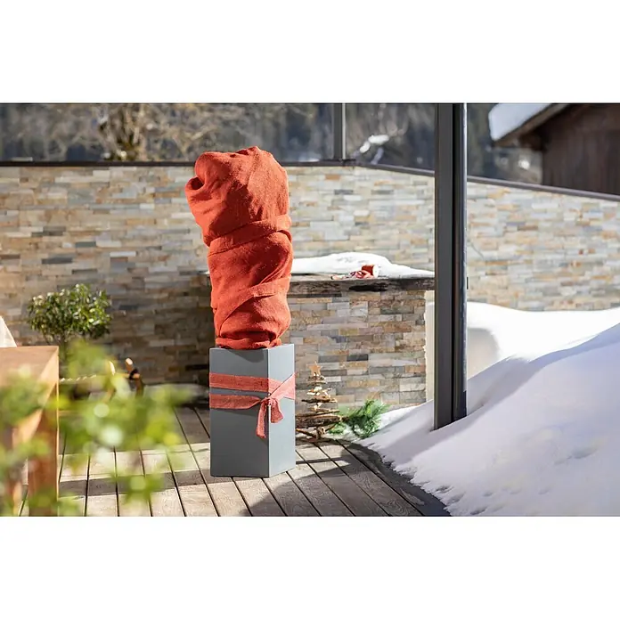 Windhager Jute-Gewebematte - Rot, L x B: 1 x 4 m, 200 g/m² - Große orangefarbene Stoffdekoration auf grauem Sockel mit festlichem Band, auf einer Holzterrasse im Winter.