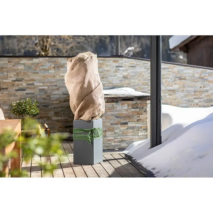 Windhager Jute-Gewebematte - 150 x 50 cm, Natur - Eine Pflanze in natürlicher Jute verpackt, mit grünem Band um einen grauen Pflanzkübel, draußen im Winter.