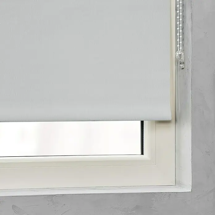 Expo Ambiente Rolloketten-Verlängerung ACC W - 3 m - Dieses Bild zeigt eine weiße Fensterjalousie, die teilweise heruntergelassen ist und vor einem Fenster hängt, neben einer grauen Wand.