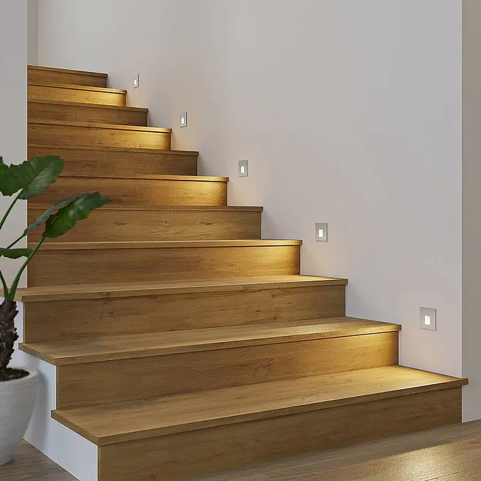 Arcchio Wandleuchte Vexi - L x B x H: 7,5 x 7,5 x 7,5 cm, alu / grau / zink - Kleine, rechteckige silberne LED-Treppenleuchten beleuchten eine moderne Holztreppe, in die Wand integriert.