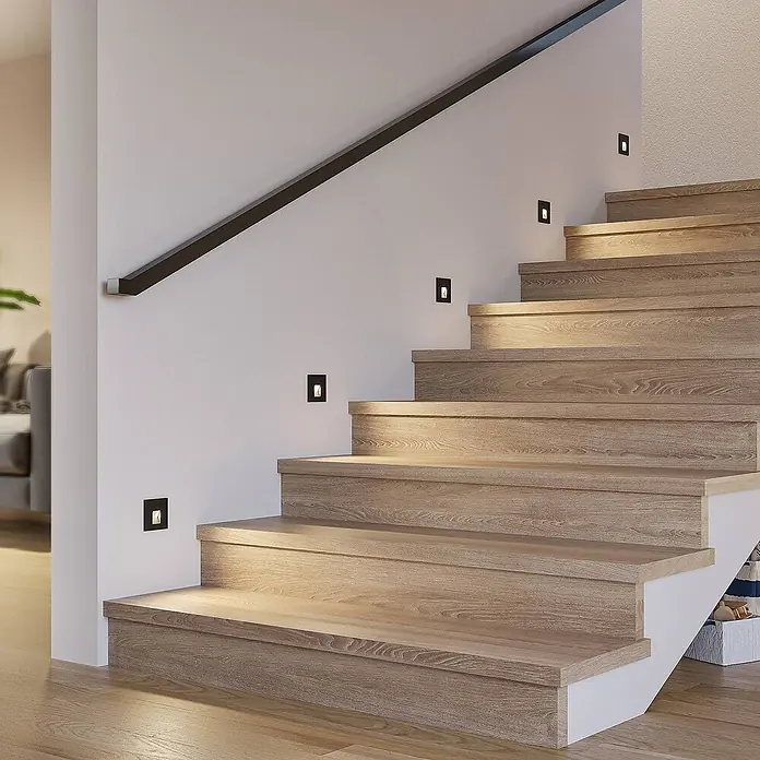 Arcchio Wandleuchte Vexi - schwarz - Schwarze quadratische Einbauleuchten beleuchten eine helle Holztreppe.