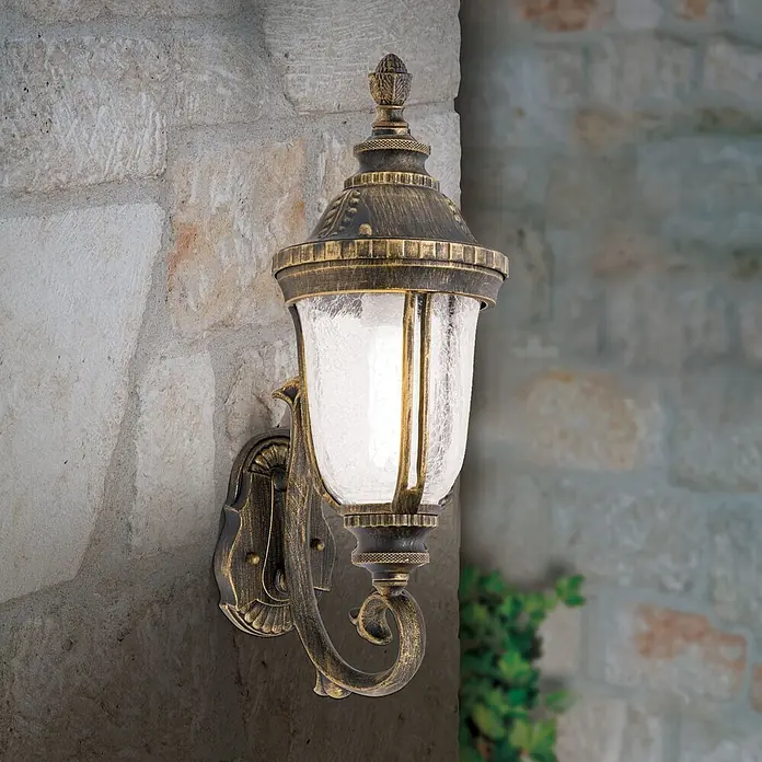 Orion Leuchten Außenwandleuchte - 24,4 x 17 x 48,7 cm, IP23 - Antike bronzene Außenwandleuchte mit Craquelé-Glas, beleuchtet und an einer Steinmauer montiert.