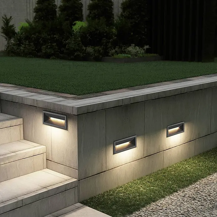 Lucande Außenwandleuchte Jaano - schwarz, IP65 - Drei dunkelgraue, rechteckige Einbaustrahler beleuchten Betontreppen und einen Gartenweg.