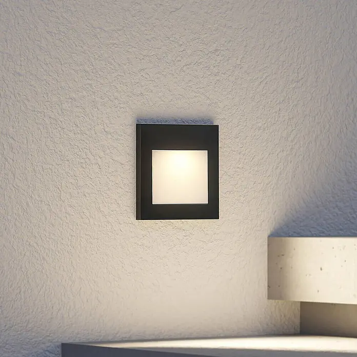 Arcchio Außenwandleuchte Zamo - schwarz, IP65 - Quadratische schwarze Wandleuchte mit warmweißem Licht, an einer strukturierten Wand montiert.