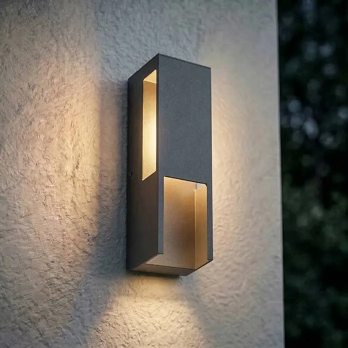 Lindby Außenwandleuchte Enyra - schwarz, weiß / opal, IP65 - Dunkelgraue rechteckige Außenwandleuchte wirft warmes Auf- und Ablicht auf eine strukturierte Wand.