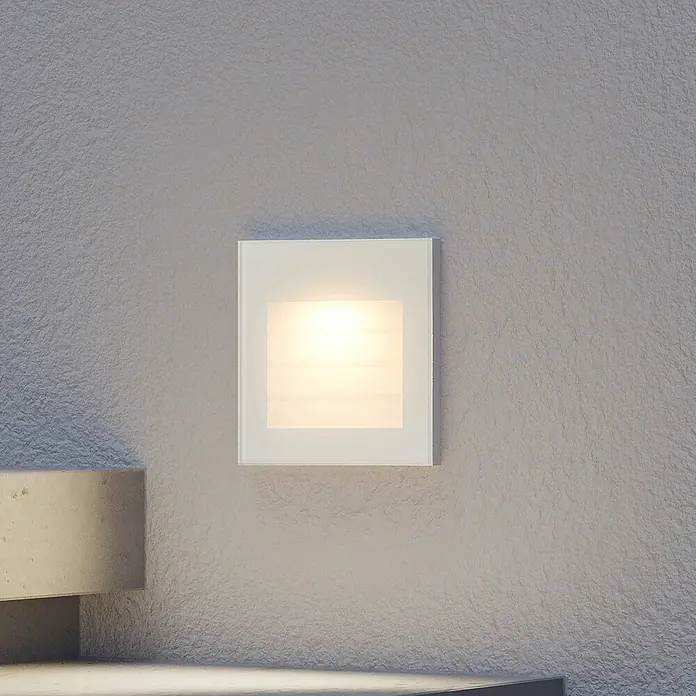 Arcchio Außenwandleuchte Zamo - weiß / opal, IP65 - Quadratische Wandleuchte mit weißer, mattierter Glasfront, die ein warmes Licht abgibt, an einer strukturierten Wand montiert.