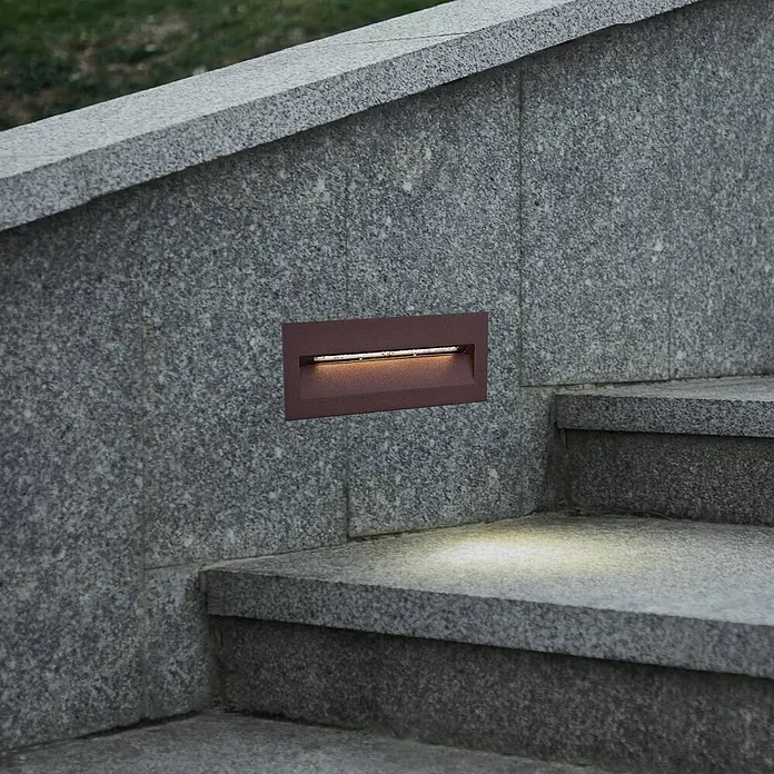 Lucande Außenwandleuchte Loya - braun / rost, IP54 - Rechteckige dunkle Bronze-Stufenleuchte in Granitwand, beleuchtet Treppenstufen.