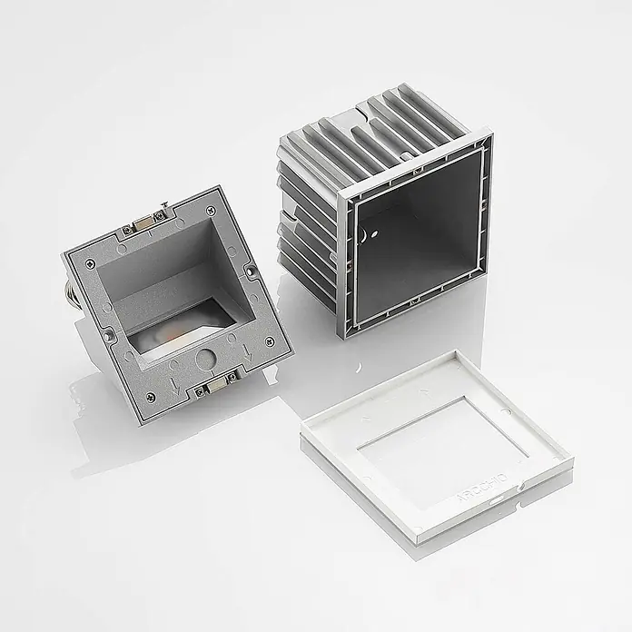 Arcchio Außenwandleuchte Zamo - weiß / opal, IP65 - Zerlegte silber-graue Aluminium-Bodeneinbauleuchte mit separatem weißem AROCCHIO-Rahmen.