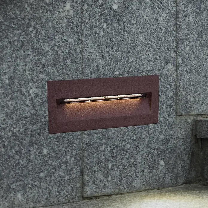 Lucande Außenwandleuchte Loya - braun / rost, IP54 - Rechteckige, dunkelbraune Einbau-Stufenleuchte in grauer Steinwand, spendet warmes Licht nach unten.