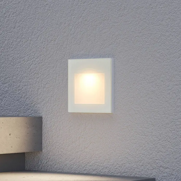 Arcchio Außenwandleuchte Zamo - weiß / opal, IP65 - Quadratische Wandleuchte mit weißem Glasrahmen, die warmes Licht auf eine strukturierte Wand wirft.