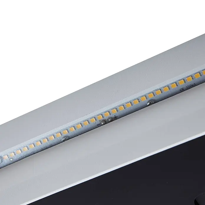 Lucande Außenwandleuchte Loya - weiß / opal, IP54 - Nahaufnahme einer silbergrauen LED-Lichtleiste mit mehreren gelb-orangen LEDs, montiert auf einer hellgrauen Oberfläche.
