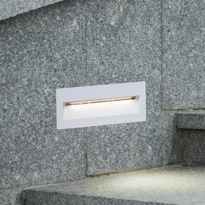 Lucande Außenwandleuchte Loya - weiß / opal, IP54 - Weißes, rechteckiges Wandeinbauleuchte in einer gesprenkelten grauen Steinwand, die Stufen beleuchtet.