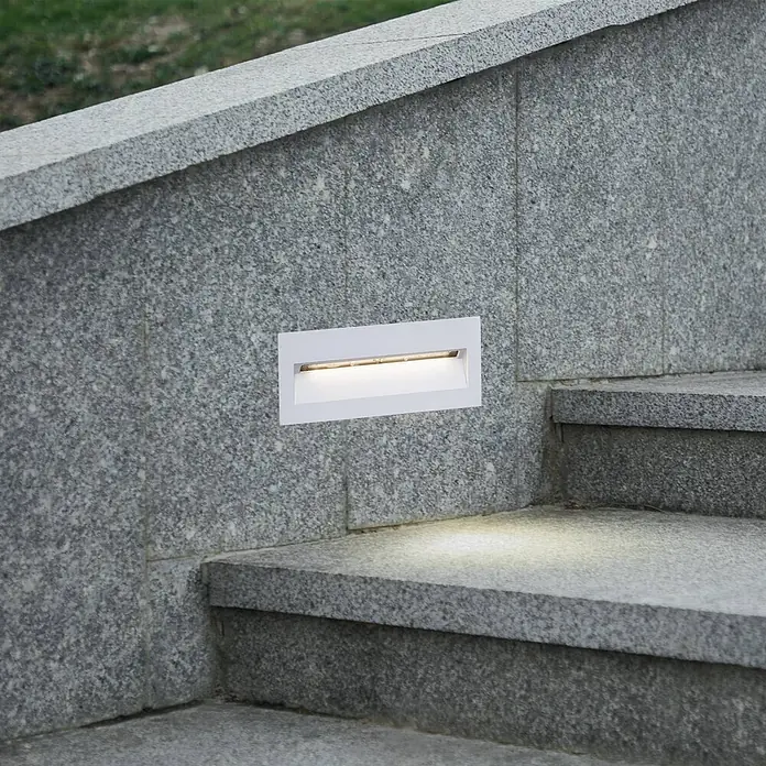Lucande Außenwandleuchte Loya - weiß / opal, IP54 - Weißes, rechteckiges Einbau-Treppenlicht in Granitwand, beleuchtet graue Stufen.