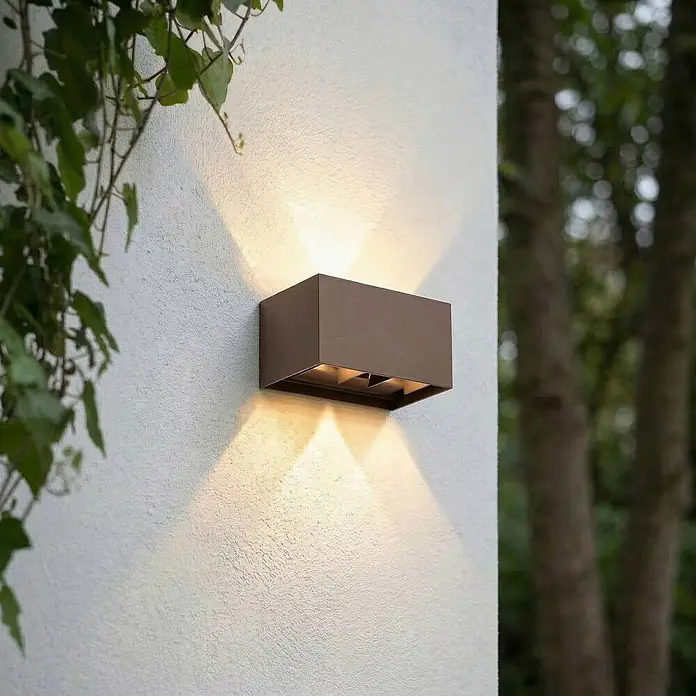 Lindby Außenwandleuchte Nivar - 10 x 20 x 10 cm, braun / rost, braun / rost, IP54 - Rechteckige, dunkelbraune Außenwandleuchte an einer strukturierten weißen Wand, die warmes Licht nach oben und unten abgibt.