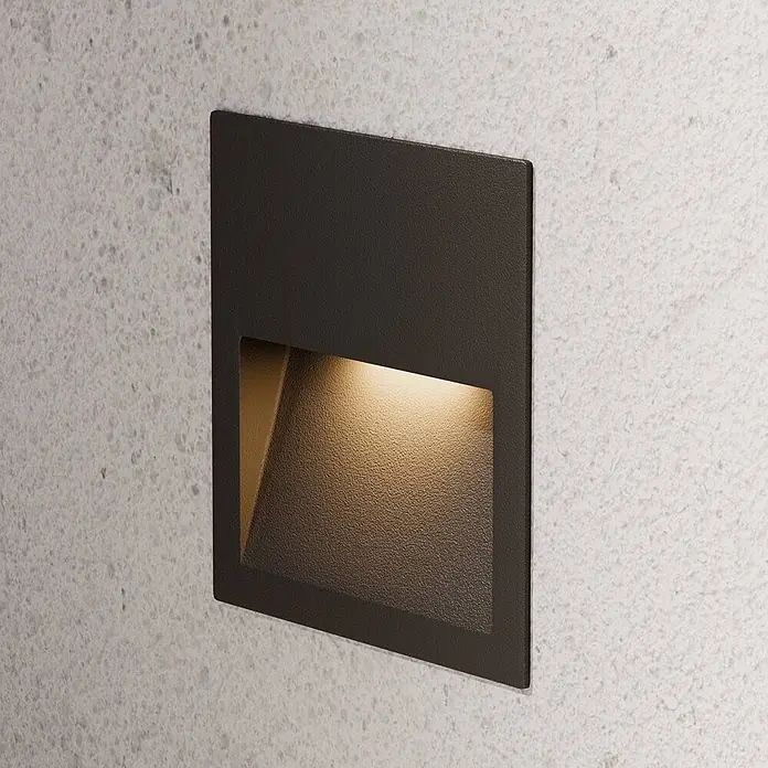 Lucande Außenwandleuchte Loya - schwarz, schwarz, IP54 - Quadratische dunkelgraue Einbauleuchte mit warmer Beleuchtung, in eine Betonwand integriert.