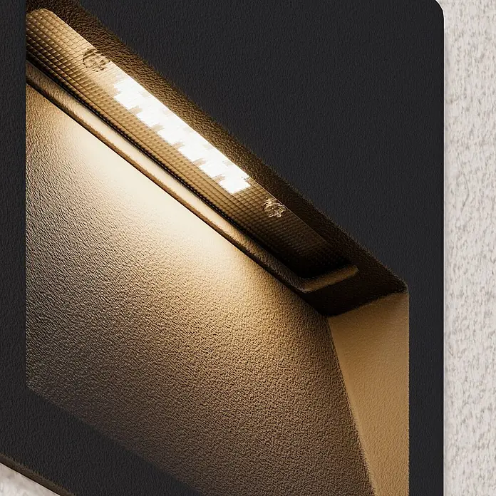 Lucande Außenwandleuchte Loya - schwarz, schwarz, IP54 - Texturierte dunkle Metall-LED-Wandleuchte beleuchtet eine texturierte Wand mit warmem Licht.