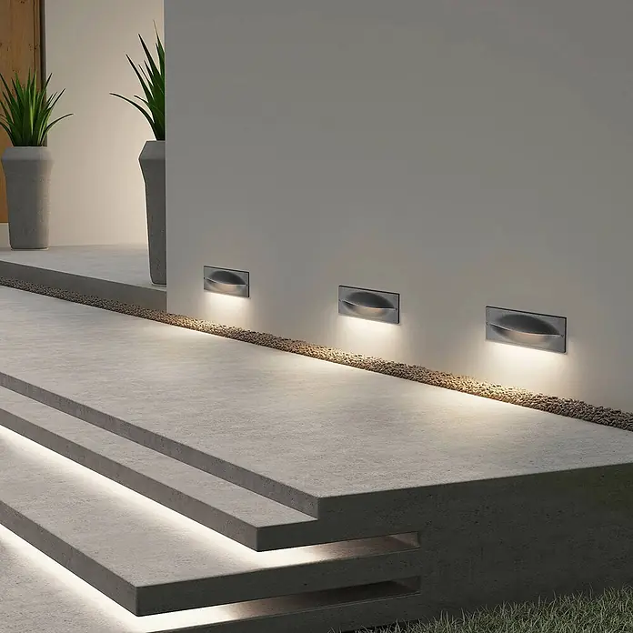 Lucande Außenwandleuchte Zandro - schwarz, IP65 - Drei rechteckige Einbauwandleuchten mit gewölbten Diffusoren beleuchten einen Außenweg und Treppen, integriert in ein modernes Betondesign.