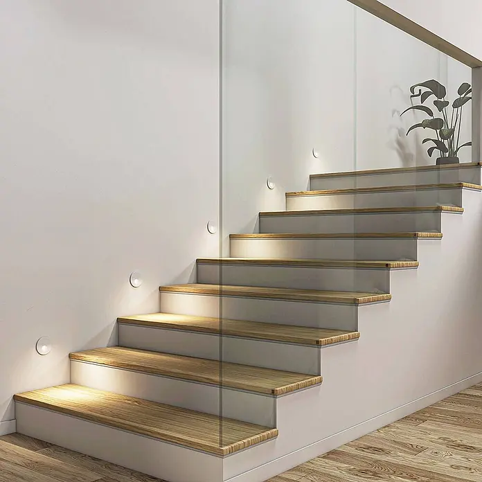 Arcchio Wandleuchte Vexi - L x B x H: 7,5 x 7,5 x 4,06 cm, weiß / opal - Runde, weiße Einbaustufenleuchten entlang einer modernen Holztreppe mit Glasgeländer, die die Stufen beleuchten.