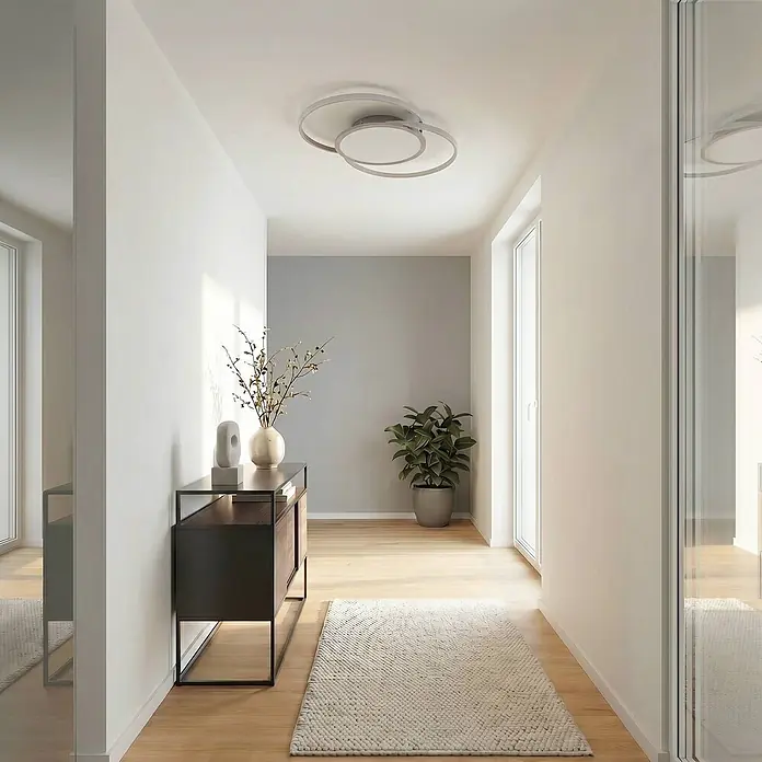 Lucande Deckenleuchte Senne - alu / grau / zink - Eine moderne Deckenleuchte mit zwei überlappenden silberfarbenen Ringen beleuchtet einen modernen Flur.