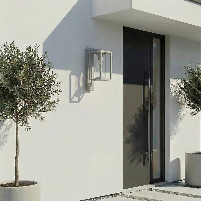Lucande Außenwandleuchte Ferda - alu / grau / zink, alu / grau / zink, IP44 - Moderne graue Außenwandleuchte mit rechteckigem Rahmen und sichtbarer Glühbirne, an der Hausfassade neben einer Tür montiert.